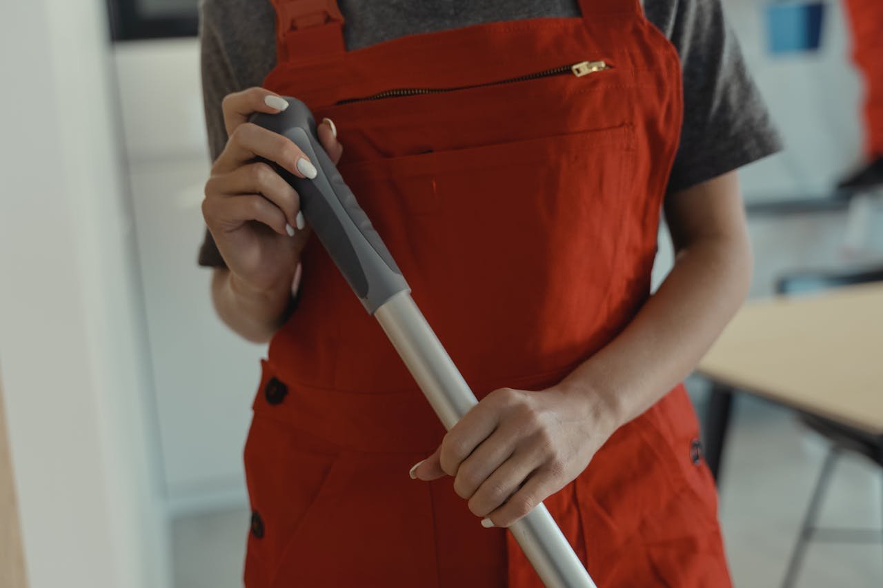 portfolio-06 A woman in a red apron holding a mop handle, performing cleaning indoors.